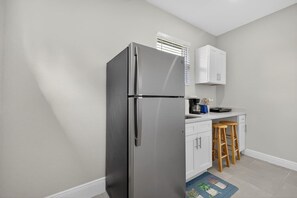 Eine kompakte Küche mit einem Edelstahlkühlschrank, weißen Schränken, einer Kaffeemaschine und Holzbarhockern.