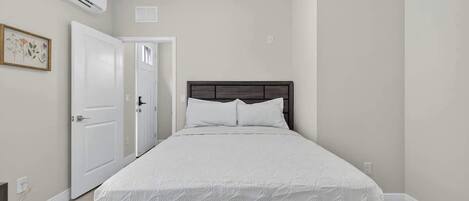 Un dormitorio con cama, paredes blancas, una puerta y un equipo de aire acondicionado.