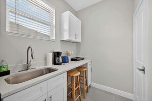 A kitchen with a sink, a coffee maker, and two wooden stools.