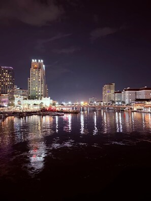 A nighttime cityscape with illuminated buildings along a waterfront.