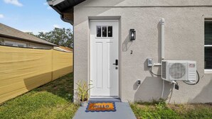Una casa con puerta blanca, ventana pequeña y un equipo de aire acondicionado en la pared exterior.