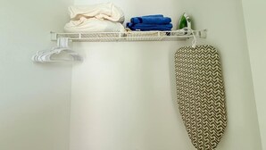 Un área de almacenamiento ordenada con un perchero, una tabla de planchar plegada y un tablero de planchar fijado a la pared.
