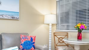 Een kamer met een bank, een stoel, een tafel met een vaas, een lamp en een raam met jaloezieën.