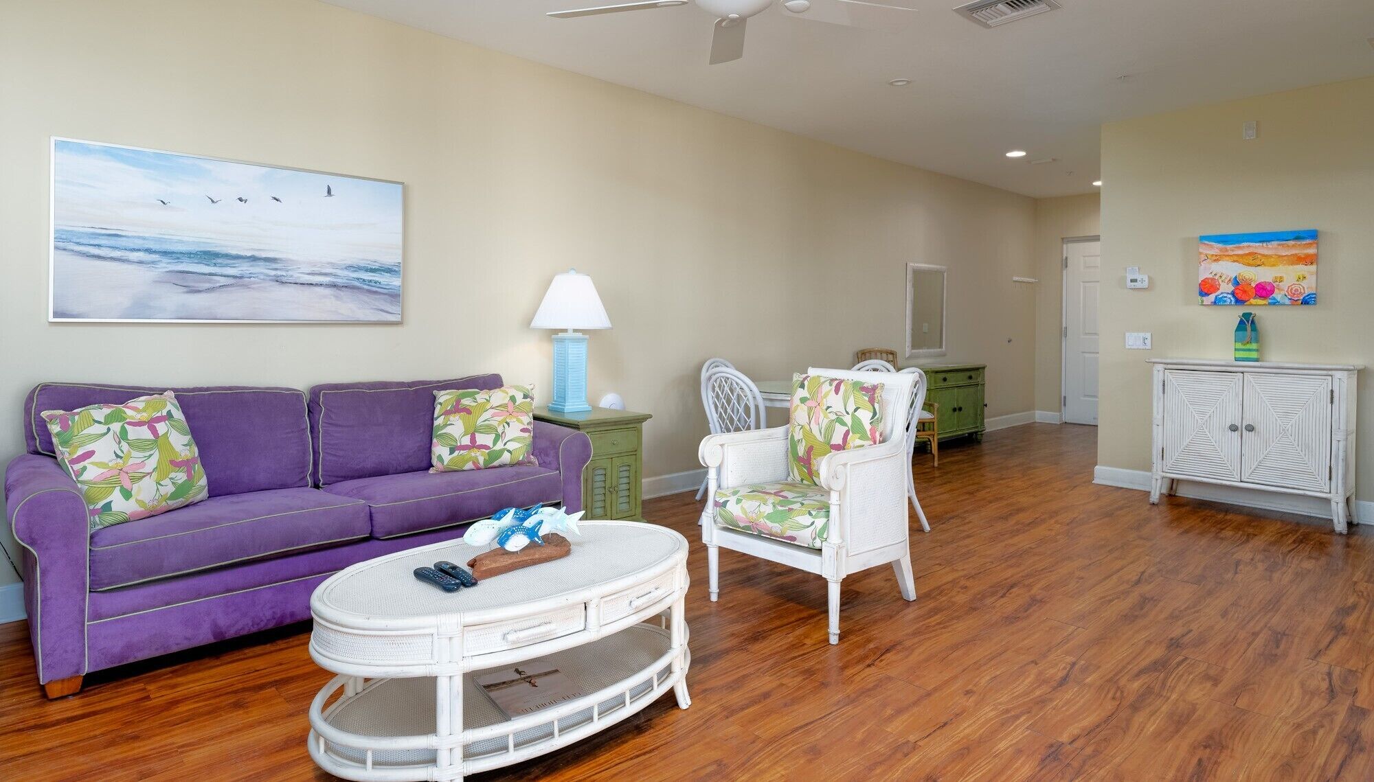 A living room with a purple sofa, a white chair, a round table, and a painting of birds.