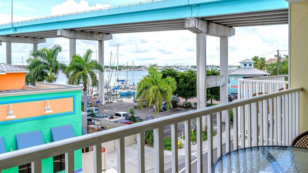 A balcony with a view of a marina, a bridge, and a building with a sign 'Upper Deck.' - Harbour House #310 "Sandpiper Retreat" (Fort Myers Beach)