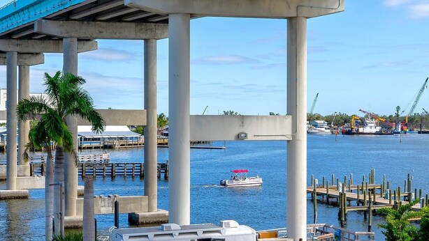 Un puente con pilares de hormigón, una marina llena de barcos y un cielo azul despejado.