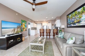 A living room with a TV, a ceiling fan, a sofa, and a coffee table. - Harbour House #312 “Castaway Dreams” (Fort Myers Beach)