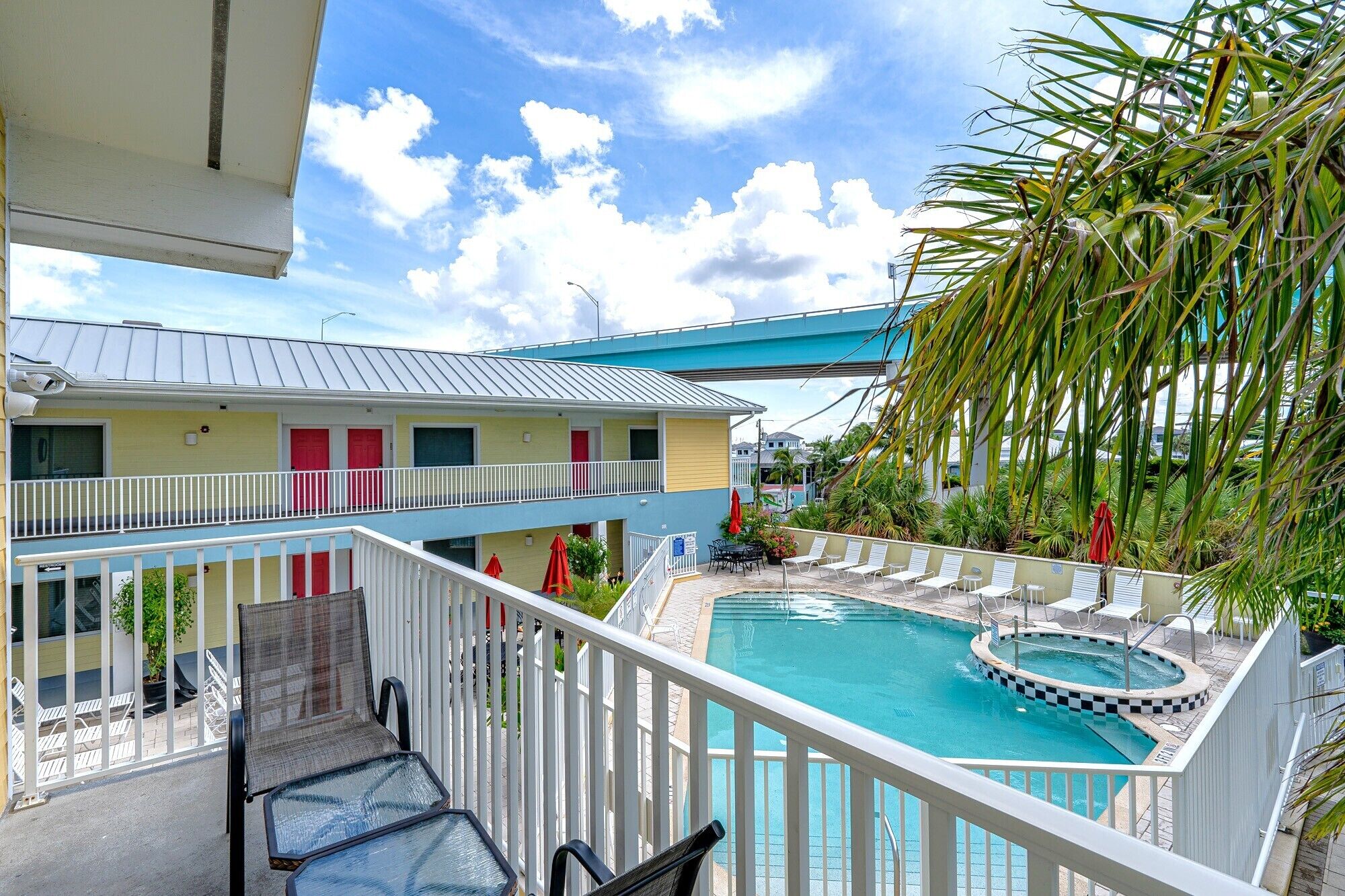 A pool area with lounge chairs, a hot tub, and a building with balconies.