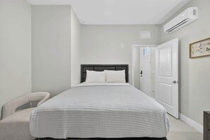 Ein Schlafzimmer mit einem Bett, einem Sessel, einer Tür und einer Klimaanlage.