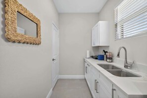 A compact kitchen with a double sink, white cabinets, and a woven mirror. - Brand-New 1BR | Minutes to Tampa’s Top Attractions (Tampa)