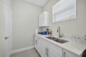 A kitchen with a white countertop, a stainless steel sink, and a window with blinds. - Brand-New 1BR | Minutes to Tampa’s Top Attractions (Tampa)