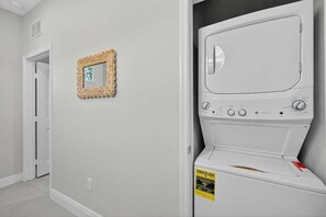 A laundry room with a white washing machine, a door, and a wall-mounted mirror. - Brand-New 1BR | Minutes to Tampa’s Top Attractions (Tampa)