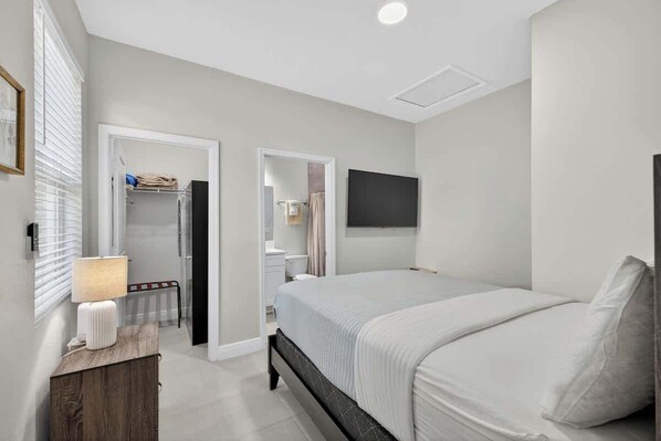 Une chambre à coucher avec un lit, une table de chevet, une lampe, une armoire et un téléviseur fixé au mur.