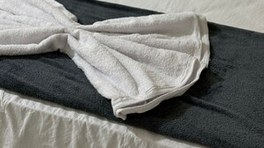 A neatly made bed with white bedding and a folded white towel on a dark-colored bed skirt. - Hotel Fazenda (Uruará)