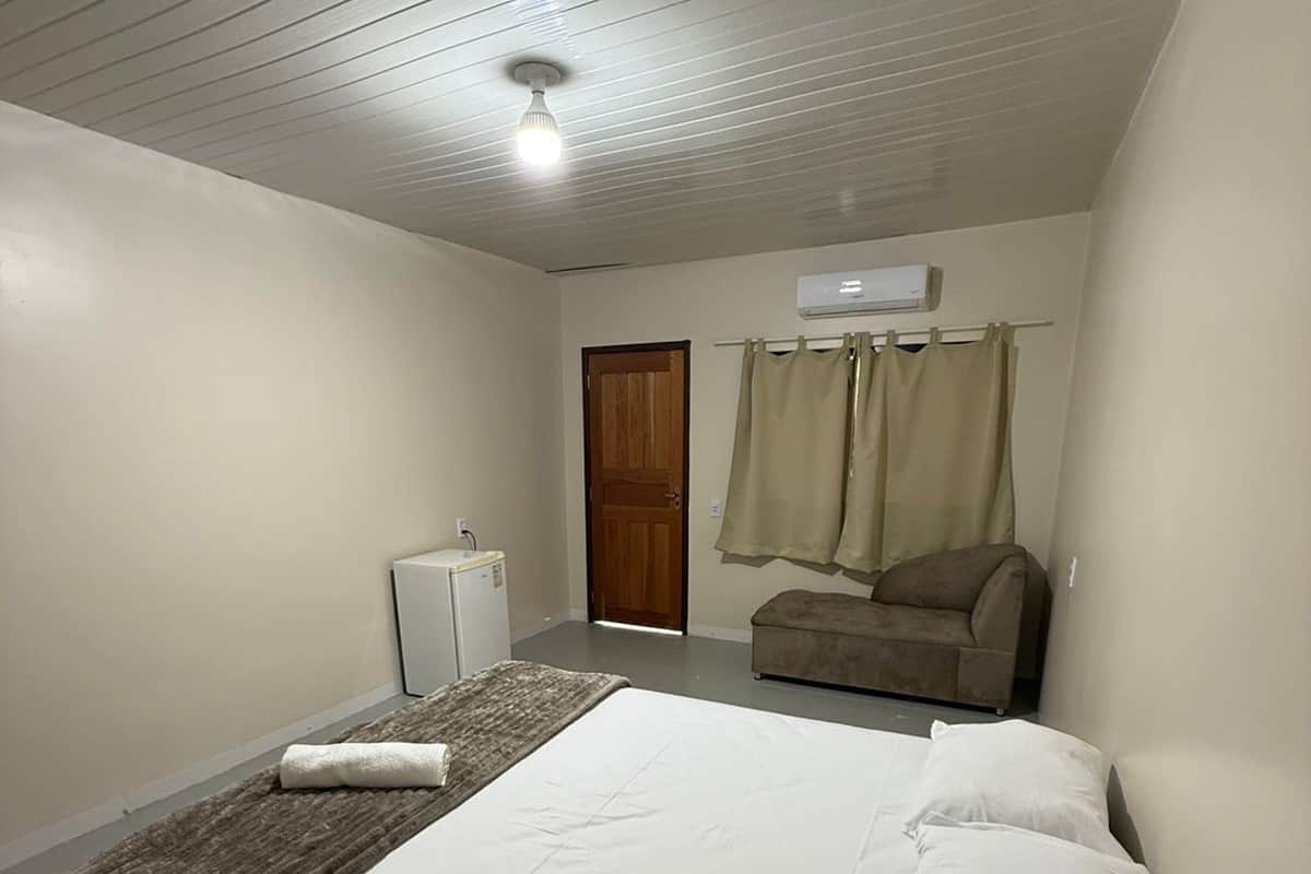 Une chambre à coucher comprenant un lit, une table de chevet, une chaise, un appareil de climatisation et une porte.