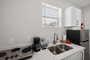 Eine moderne Küche mit Einbauherd, Kaffeemaschine, Spüle und einem Fenster mit Jalousien.
