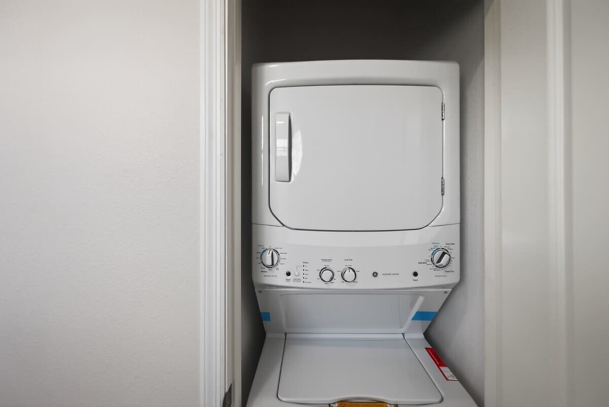 Une petite machine à laver blanche à chargement frontal, installée dans une petite buanderie avec une porte et un mur blancs.
