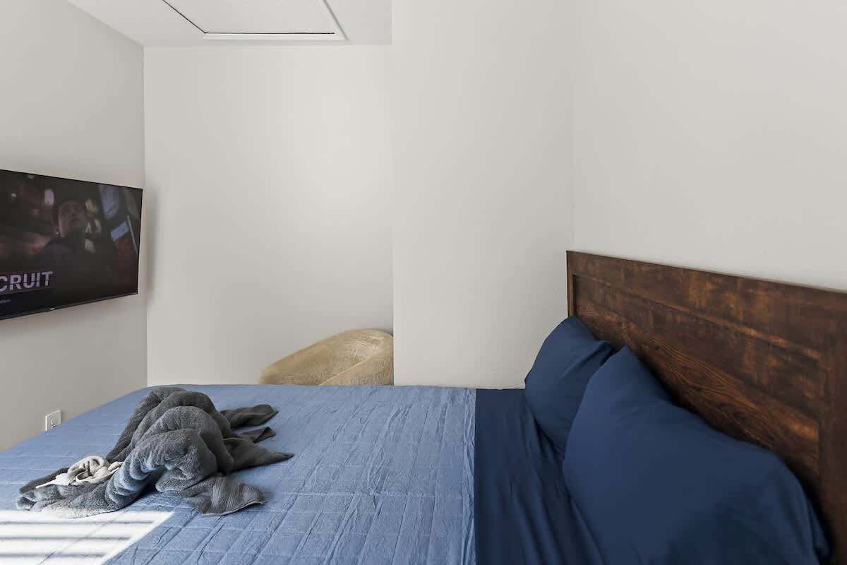 A bedroom with a bed, a television mounted on the wall, and a wooden headboard.
