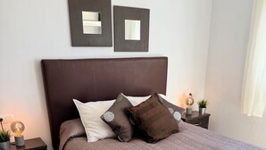 A neatly made bed with a headboard, two bedside tables with lamps, and a wall-mounted mirror. - Oasis view (Oria)