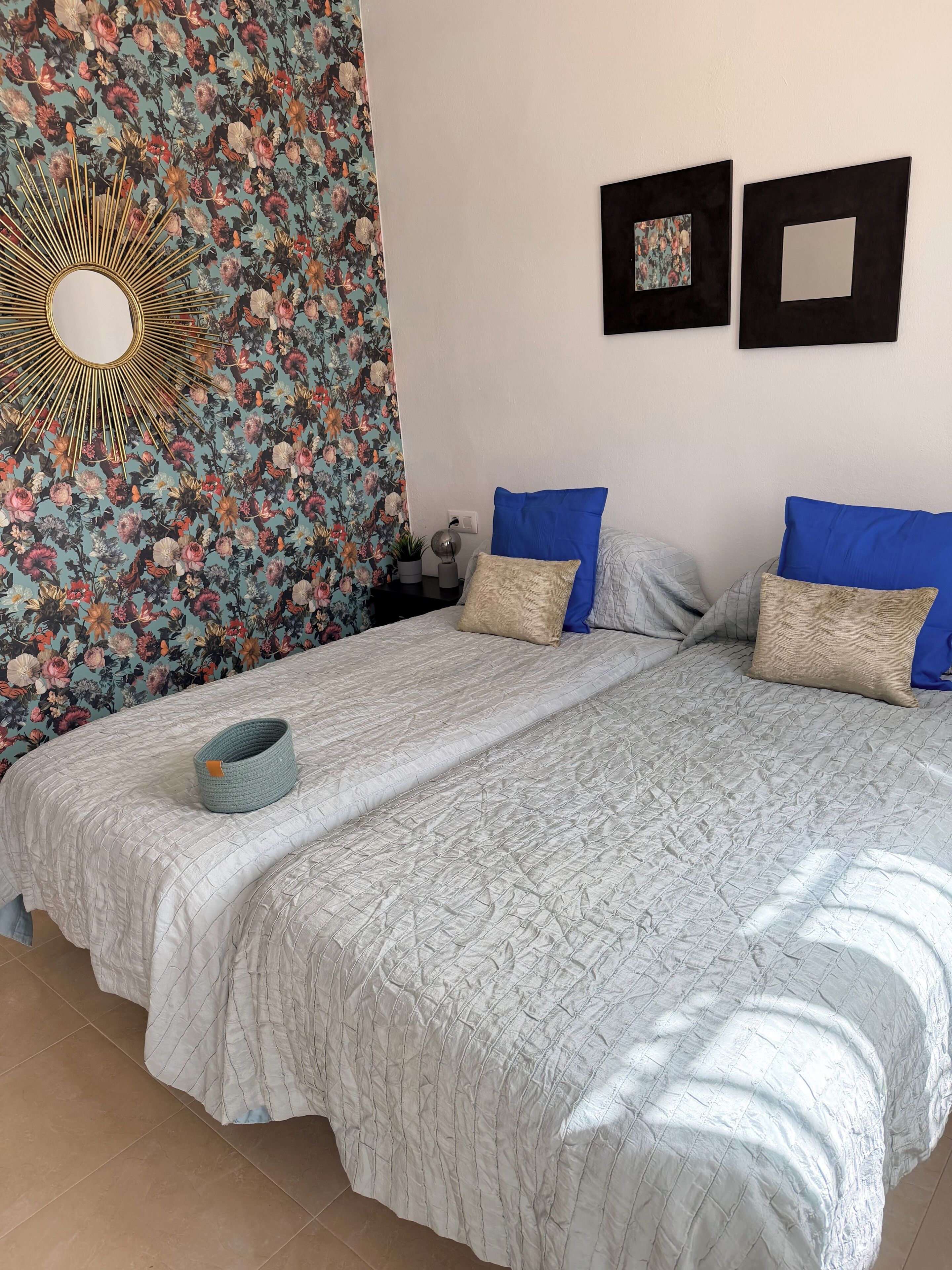 Una cama bien hecha con cubreacolchado, dos almohadas azules y una almohada decorativa color beige.