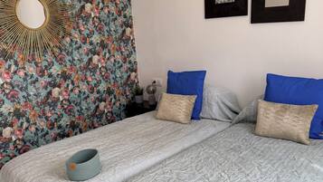 Una cama bien hecha con cubreacolchado, dos almohadas azules y una almohada decorativa color beige.