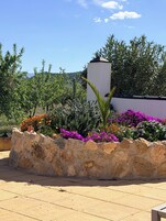 A stone planter with colorful flowers, a white wall, and a clear blue sky.