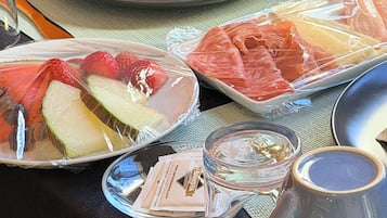 Une table avec une assiette de fruits coupés, un plat de viande emballé, un verre et une serviette sur une nappe sombre.