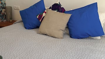A bed with a textured white cover, blue and beige pillows, and a floral-patterned wall.