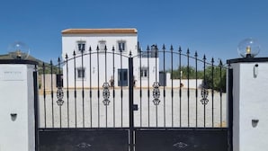 A gated entrance with a white building in the background. - Oasis view (Oria)