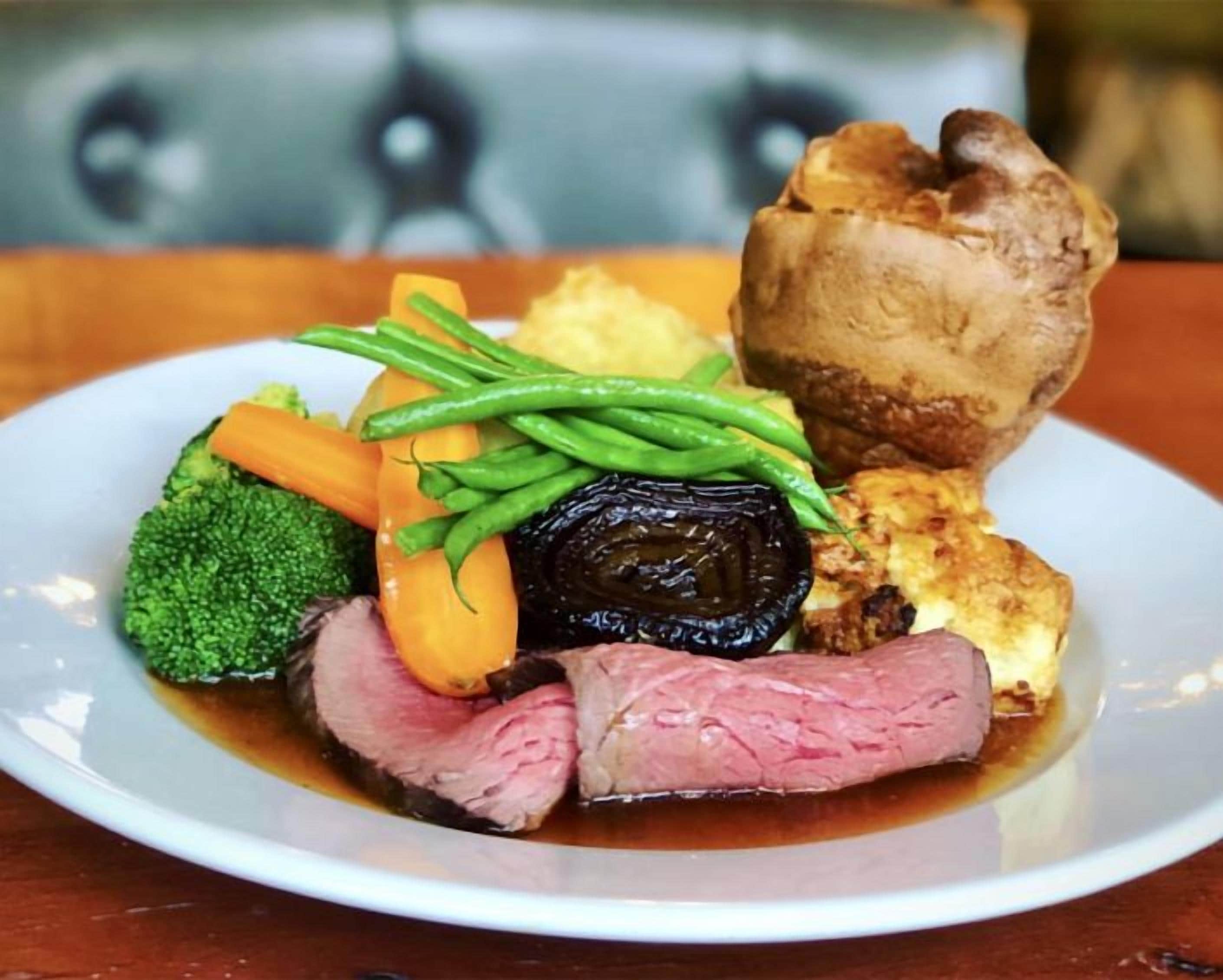 A plate with a slice of meat, vegetables, and a baked item.
