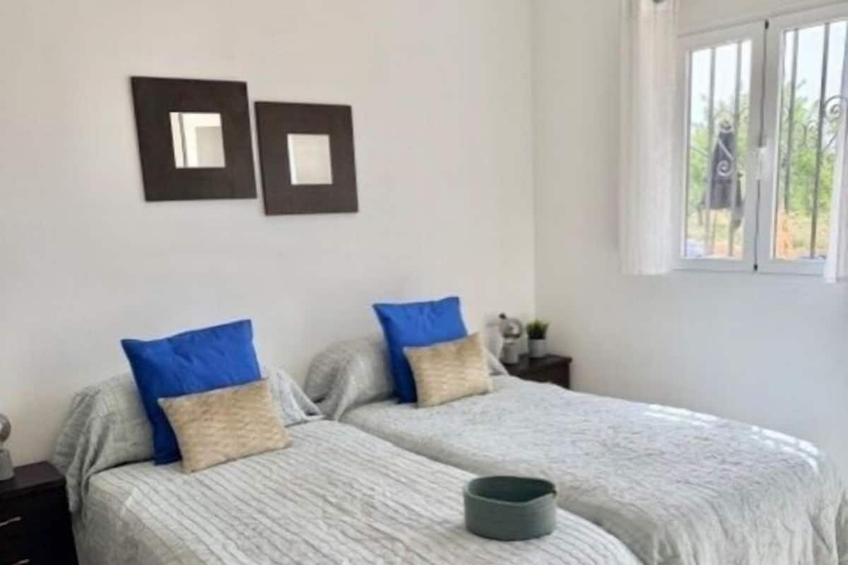 A bedroom with two beds, a window, and a small table.