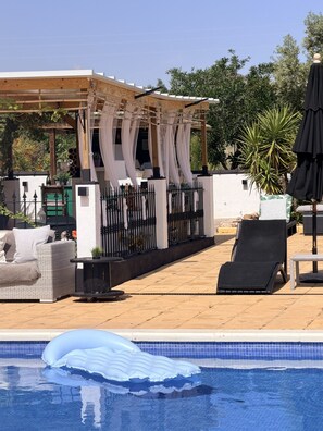 A pool area with a pergola, lounge chairs, and a fenced garden. - Oasis view (Oria)