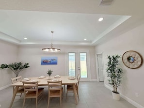 A dining area with a table set for four, a hanging light fixture, a potted plant, and a framed picture on the wall.