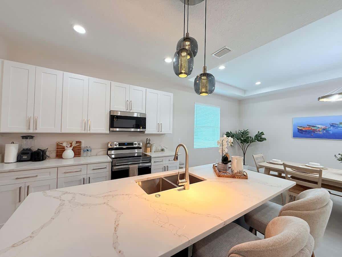 Une cuisine moderne avec des meubles blancs, un îlot central doté d’un évier et des luminaires suspendus.
