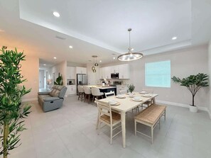 A modern kitchen with white cabinets, a dining area with a table and chairs, and a seating area with a sofa and a recliner. - Modern 3BR Home | Near Busch Gardens & Downtown (Tampa)