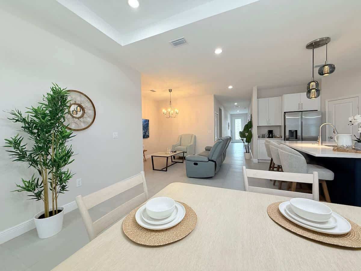 Une cuisine moderne avec des meubles blancs, un coin repas avec une table dressée pour deux personnes, et un salon avec un canapé et des fauteuils.