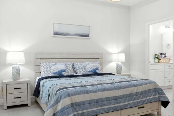 A bedroom with a bed, two bedside tables, a nightstand, a wall-mounted lamp, and a framed picture.