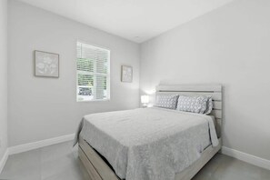 Ein Schlafzimmer mit einem Bett, einem Fenster mit Jalousien und zwei Bildern an der Wand.