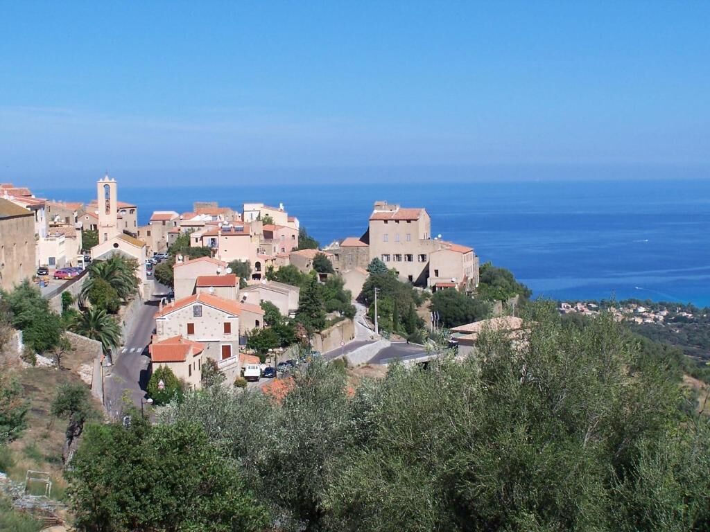 A coastal village with stone buildings, a prominent tower, and a clear view of the sea.