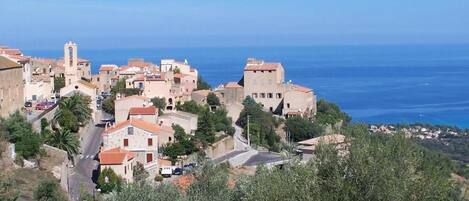 A coastal village with stone buildings, a prominent tower, and a clear view of the sea.