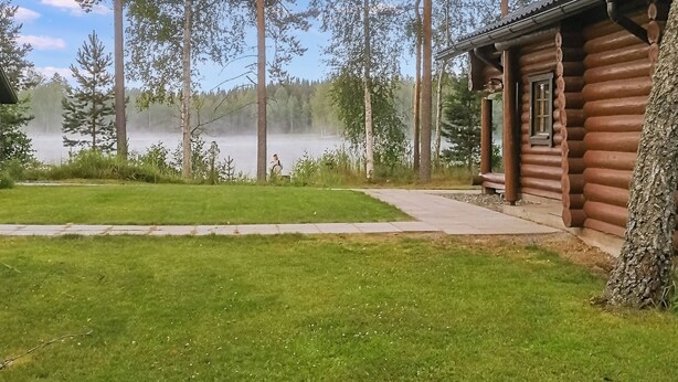 A cabin with a log exterior, a grassy yard, and a lake with mist. - Sinikello by Interhome (Pertunmaa)