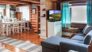 A cozy cabin interior with a dining area, sofa, TV, and wooden walls. - Sinikello by Interhome (Pertunmaa)