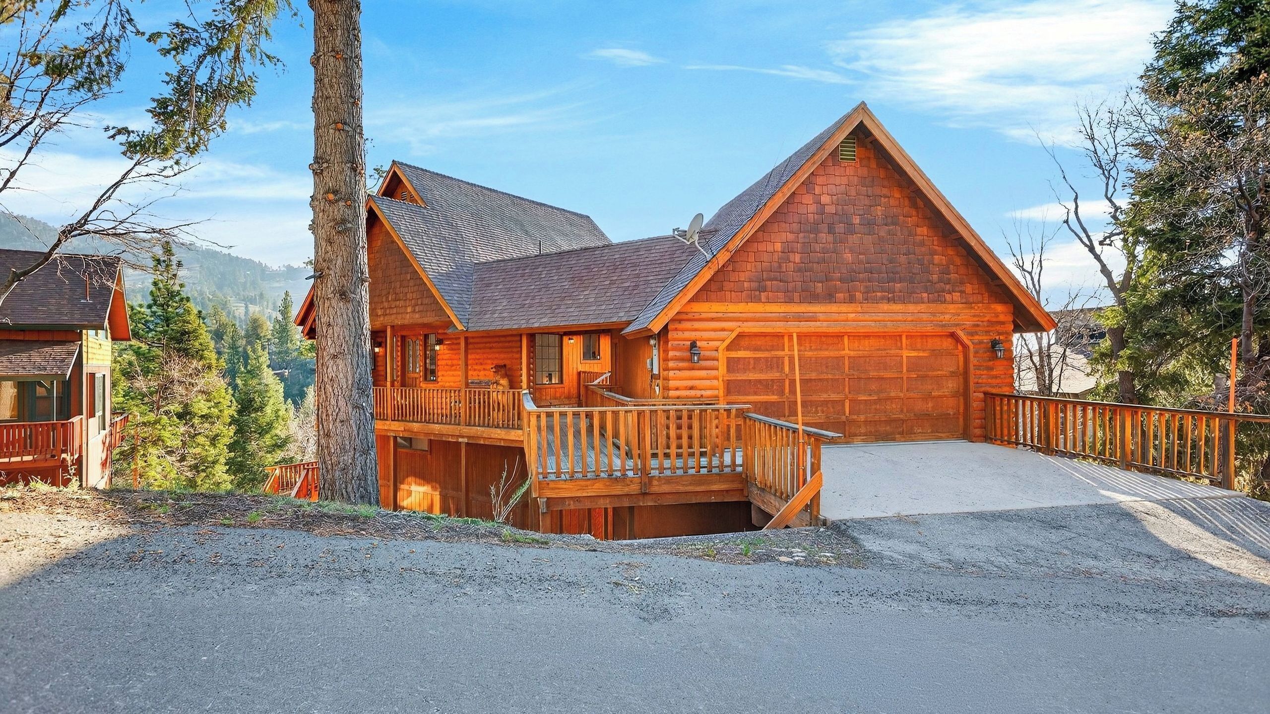 A log cabin with a deck, a garage, and a mountain backdrop.