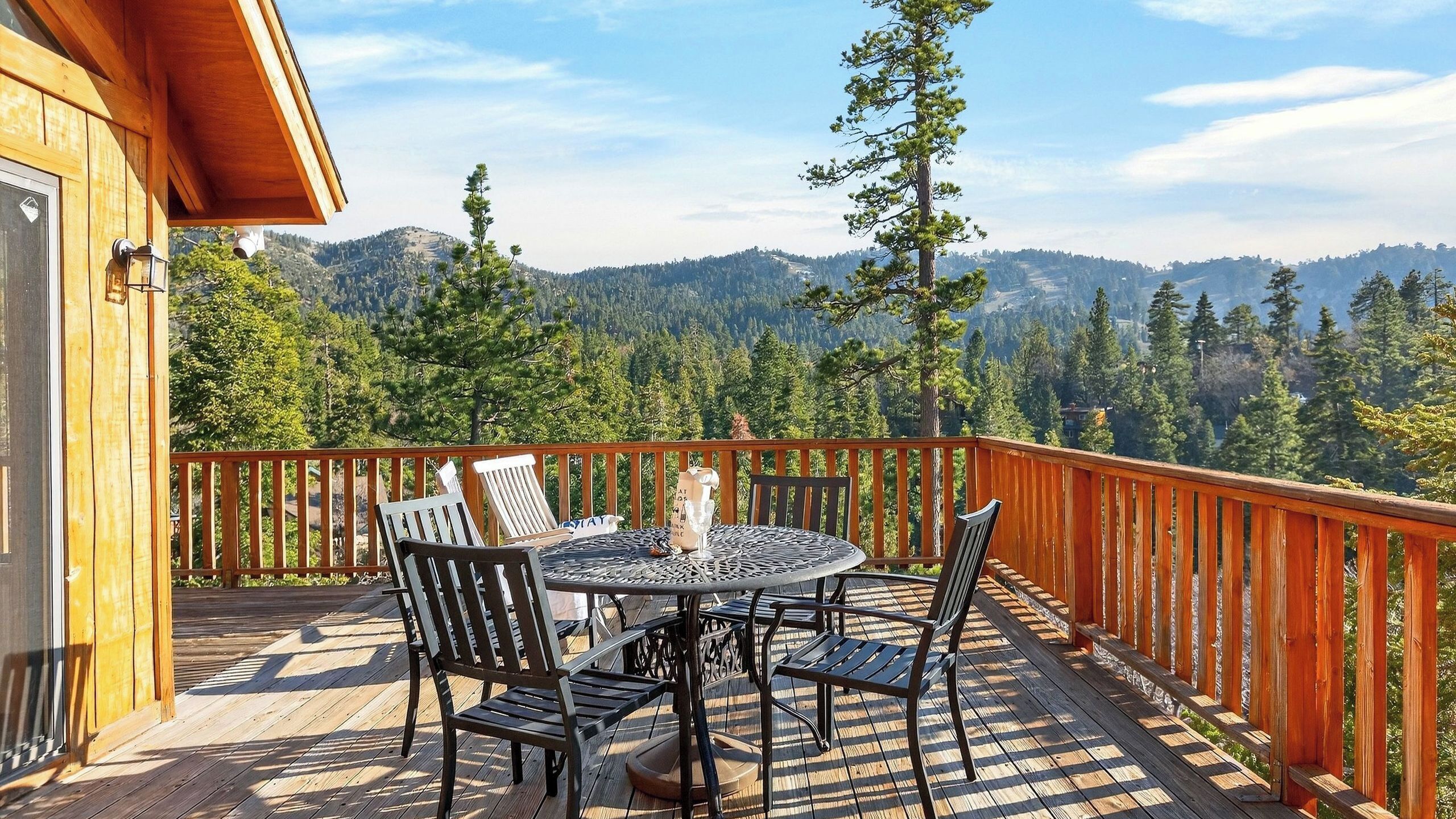 Une terrasse en bois avec une table ronde et des chaises, offrant une vue sur une chaîne de montagnes boisée.