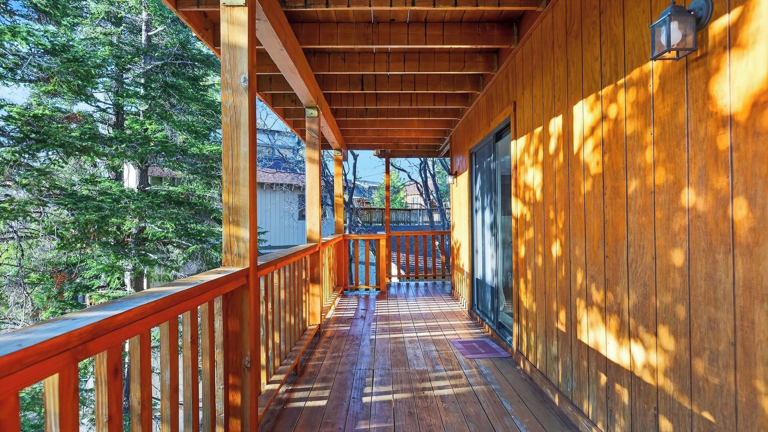 A wooden deck with a railing, leading to a covered area with a door and windows.