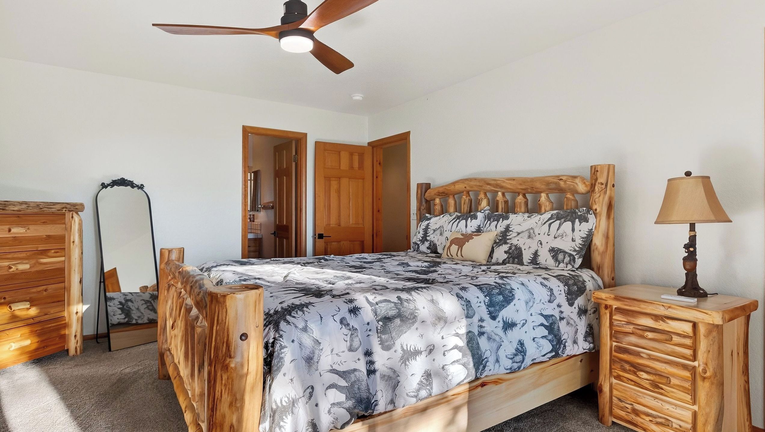 A bedroom with a wooden bed, a ceiling fan, a bedside lamp, and a mirror.