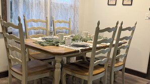 A dining table set with chairs, a window with patterned curtains, and two framed signs on the wall. - 3-bedroom house in Shiloh ,enjoy a peaceful stay in the country. (Shiloh)
