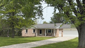 A single-story brick house with a covered porch, a garage, and a gravel driveway. - 3-bedroom house in Shiloh ,enjoy a peaceful stay in the country. (Shiloh)