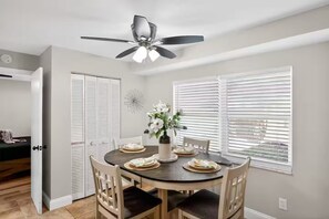 A dining area with a round table, white chairs, a ceiling fan, and a window with blinds. - Beautiful 4/2 house, minutes from Busch Gardens (Tampa)