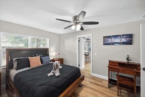 Un dormitorio con cama, escritorio, ventilador de techo y vistas a un balcón.